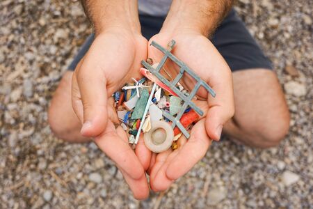 Man sitting on the beach and Holding with his two hands Plastic and Micro plastics waste and garbage from the sea and the sand. Ecofriendly, Sustainability, Ecologic and Plastic Free Concept.の写真素材