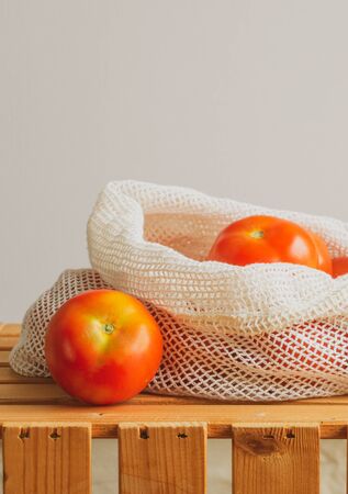 Eco friendly and no plastic concept. Reusable Cotton Mesh Bag full of tomatoes isolated on white on top of a wooden fruit box.の写真素材