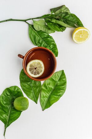 Fresh lemon water drink in a clay cup with some lemon tree leaves, lime and a lemon on the background isolated on white. Fresh summer background.の写真素材