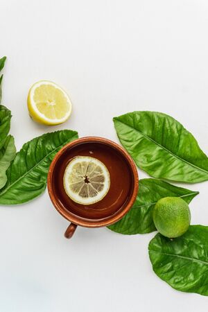 Fresh lemon water drink in a clay cup with some lemon tree leaves, lime and a lemon on the background isolated on white. Fresh summer background. Top View.の写真素材