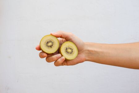 Hand holding a sliced yellow kiwi isolated on white wall.の写真素材