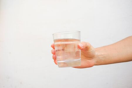 Hand holding a transparent glass full of water isolated on a white wall.の写真素材