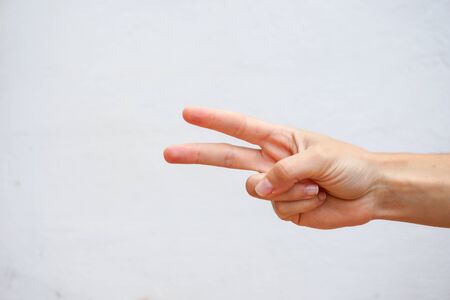 Hand with two fingers up in the peace, victory symbol or the letter V in sign language. Isolated on a white wall texture. Close up view.の写真素材