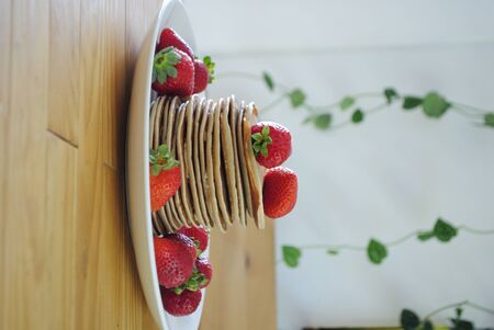 stack of pancakes with some organic and fresh strawberries with some green plants on the background. Sweet and tasty food concept.の写真素材