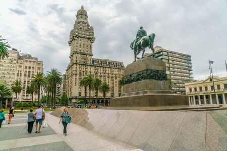 Tourists passing the statue of General Artigas on the Independance square (Plaza Indepencia) with in the background the famous Salvo Palace (Palacio Salvo), Montevideo, Uruguay, January 25th 2019のeditorial素材