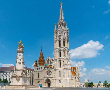 Budapest, Hungary - June 27th 2020 - Exterior of the Matyas Templom (Matthias Church), with the Szentharomsag-szobor (Holy Trinity Statue) in front during Corona time on a sunny day with some tourists visiting the churchのeditorial素材