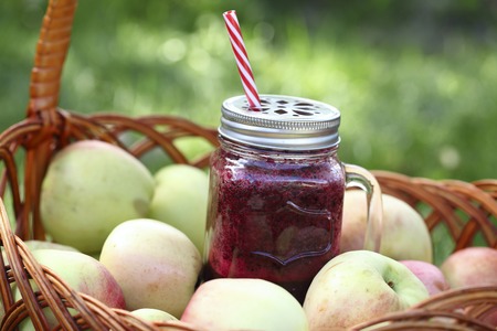 Berry smoothie in a basket on a pile of apples. On the background of sunlight and grassの写真素材