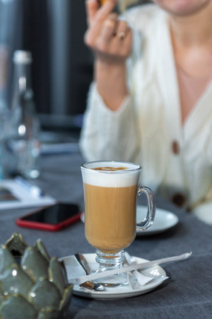 a glass of latte on a saucer. A girl is sitting at the table. face is not visibleの写真素材