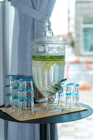 water in glassware in the form of a samovar near the window on the table. Lemon slices and mint leaves float in it.の写真素材