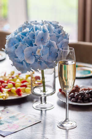 beautiful blue hydrangea near a glass of sparkling wine on a festive tableの写真素材