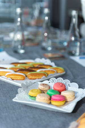 several colorful macarons in a plate with an openwork napkin. Eclairs with white, brown and green glazeの写真素材