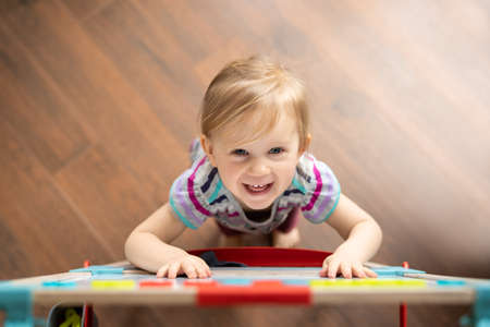 smiling happy two year old girl looking up at camera while standing next to easel magnetic boardの写真素材