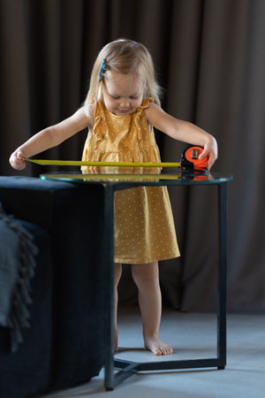 A little two-year-old girl measures the length of the table with a tape measureの写真素材