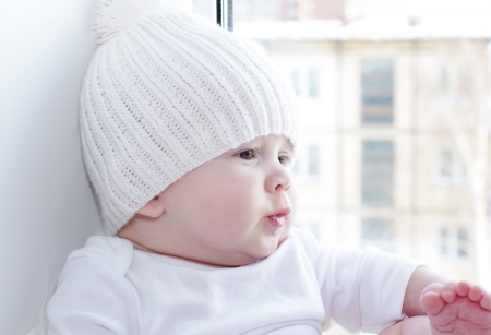 The baby sits at a window overlooking the next house 