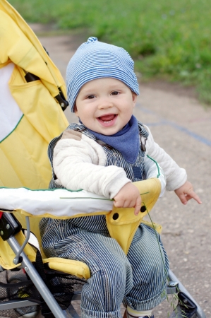 happy baby boy on yellow baby carriage outdoorsの写真素材