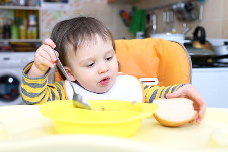16 months baby eating soup and breadの写真素材