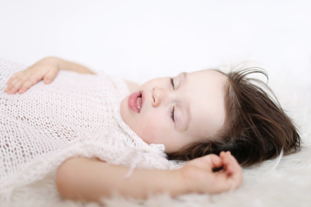 portrait of 2 years lovely child sleeping on white fur plaidの写真素材