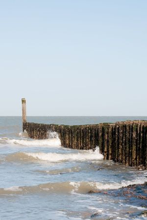 Breaking the waves at the beach with wooden polesの写真素材