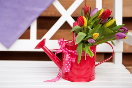 Decorative pink watering can with cheerful bouquet tulips on bench outdoorの写真素材