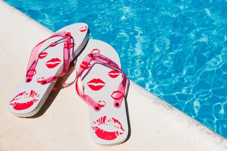 Flip flops near the swimming pool with blue waterの写真素材
