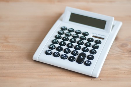 White calculator on wooden desk with sun cellsの写真素材