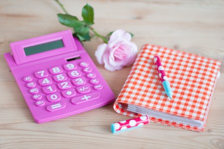 Pink calculator and notice book with dotted pencils on wooden deskの写真素材