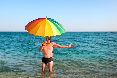 Elderly man standing in swimming trunk at the sea under the umbrellaの写真素材