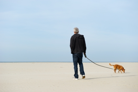 Lonely elderly man with dog at the beach の写真素材