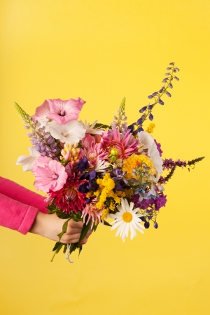 Holding mixed garden bouquet flowers on yellow backgroundの写真素材