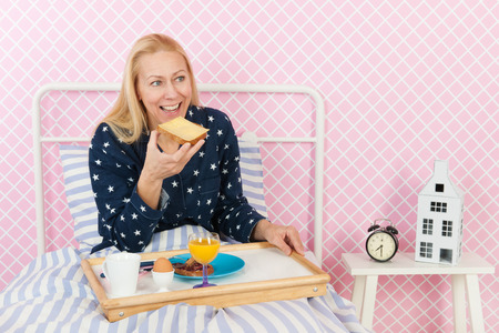 Middle aged woman is having breakfast in bedの写真素材