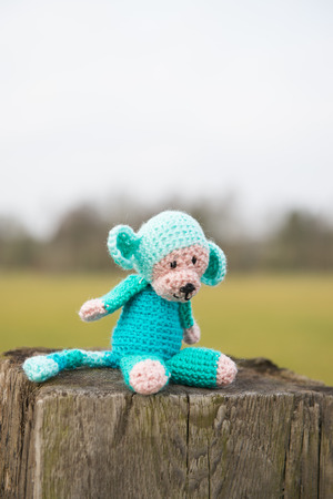 crocheted selfmade monkey toy sitting on fence outdoorの写真素材