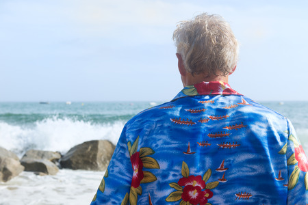 Senior man looking at the sea with surfs on the rocksの写真素材