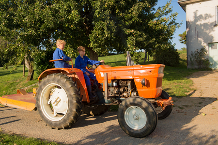 Farm boys riding on orange tractorの写真素材