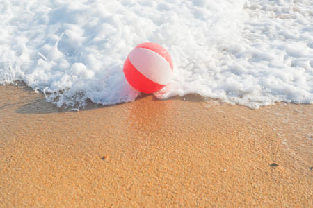 Red and white beach ball playing with the surf and the sea at the beachの写真素材