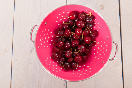 Fresh washed cherries in pink colander on wooden undergroundの写真素材