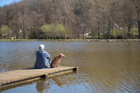 Man sitting with his dog on landing stage at nature lakeの写真素材
