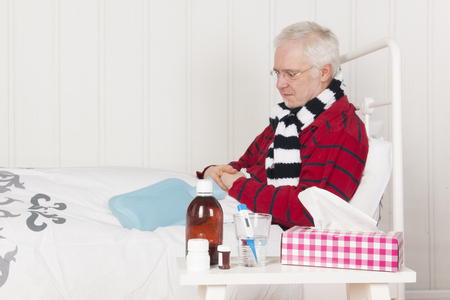Senior sick man sitting in bed with medicinesの写真素材