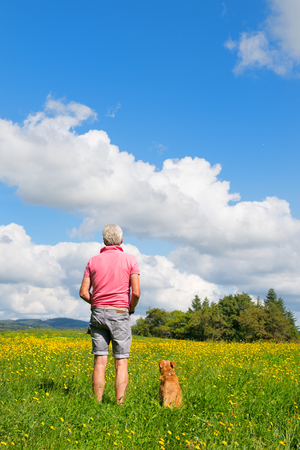 Senior man sitting with dog in landscapeの写真素材