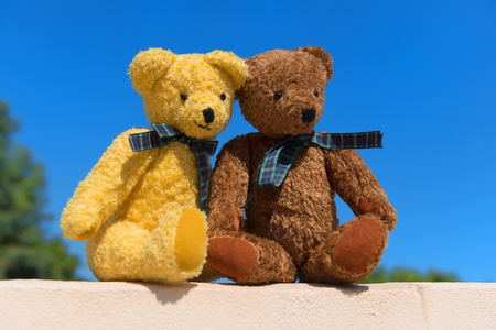 Two toy bears in love on wall in front of blue skyの写真素材