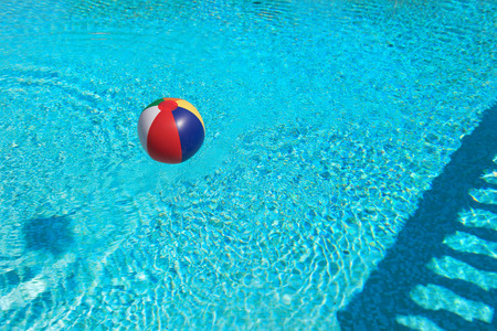 Inflatable colorful beach ball floating in water from swimming poolの写真素材