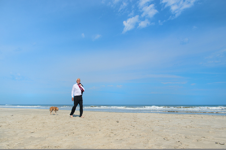 Business man in formal suit walking his dog at the beachの写真素材