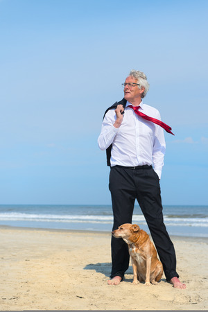Business man in formal suit standing with his dog at the beachの写真素材