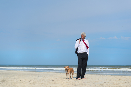 Business man in formal suit walking his dog at the beachの写真素材