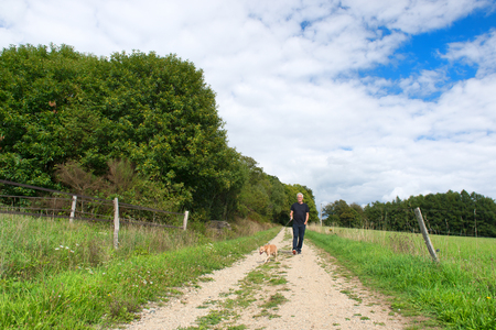 Senior man walking the dog on little lane in natureの写真素材