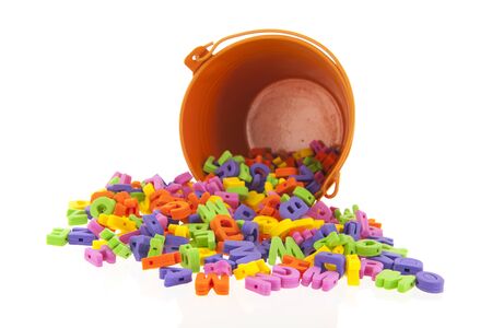 Fallen orange bucket with many foam letters isolated over whiteの写真素材