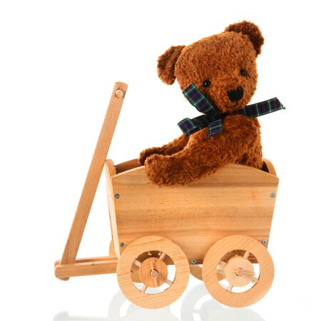 Stuffed bear toy with bow sitting in wooden cart isolated over whiteの写真素材