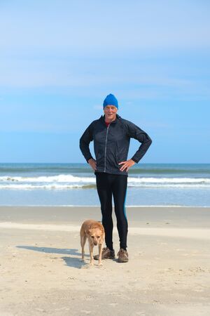 Healthy senior man as runner with his dog at the beachの写真素材