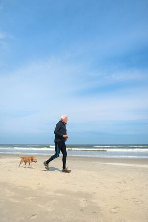 Healthy senior man as runner active with his dog at the beachの写真素材
