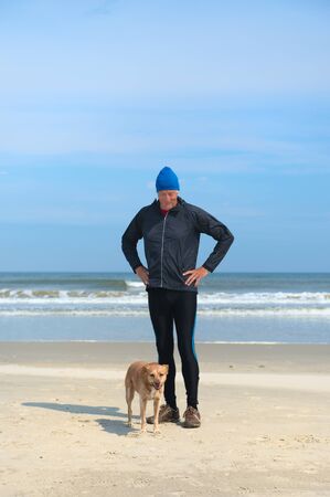 Healthy senior man as runner with his dog at the beachの写真素材