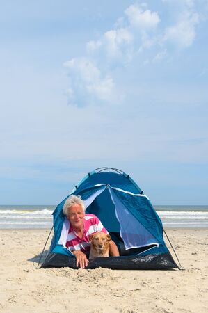 Single senior man with his dog camping in shelter at the beachの写真素材